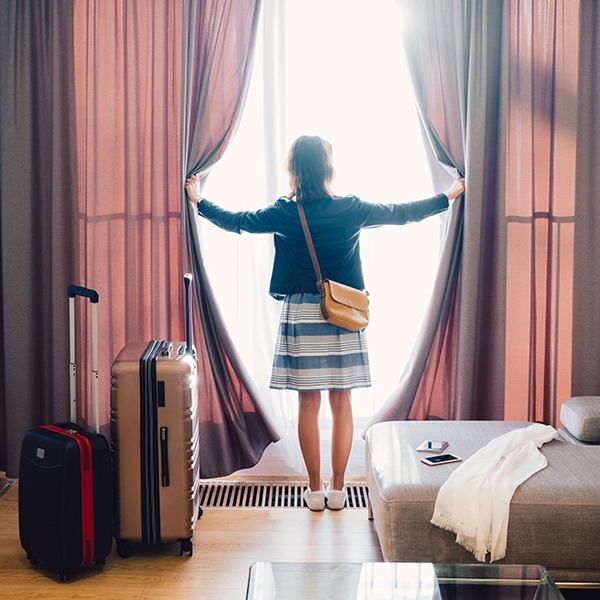 woman pulling curtains back in hotel room with suitcases